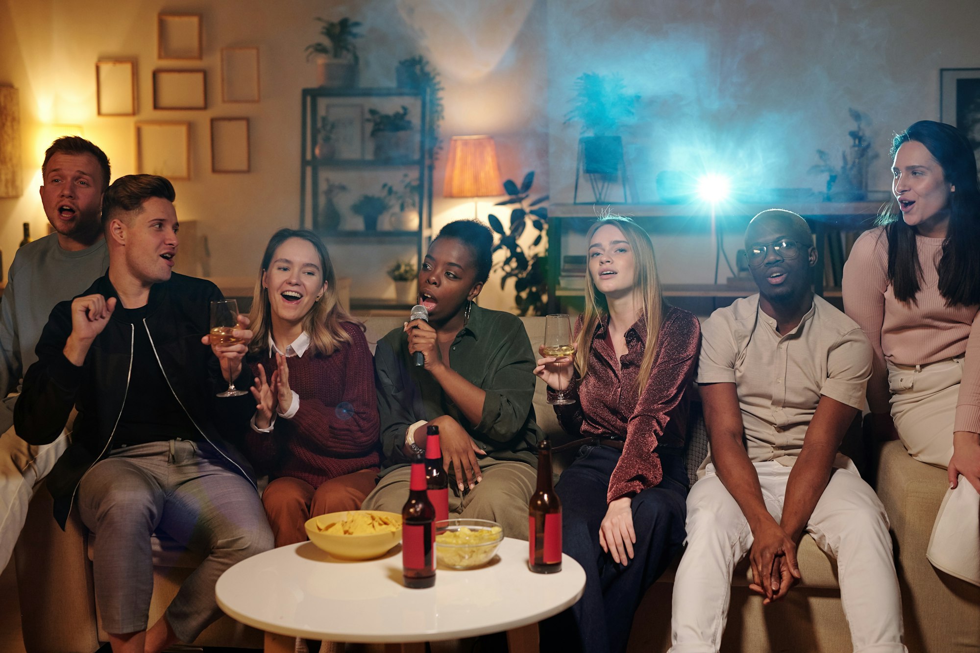 Group of young intercultural friends singing karaoke while sitting on couch